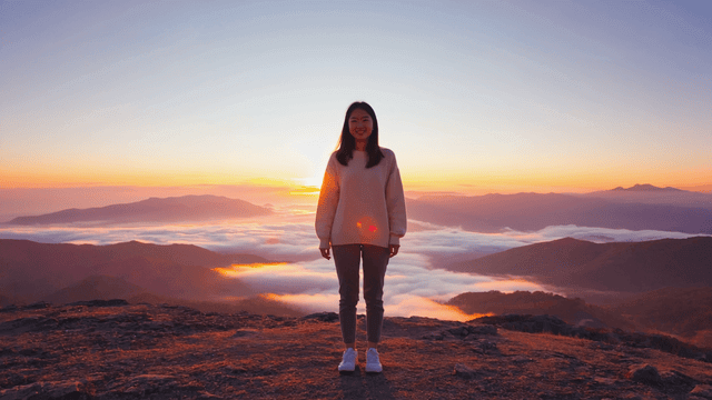 A person, female, with a serene expression, standing on a mountaintop at sunrise, symbolizing new beginnings and optimism. The scene should convey a sense of peace, freedom, and excitement